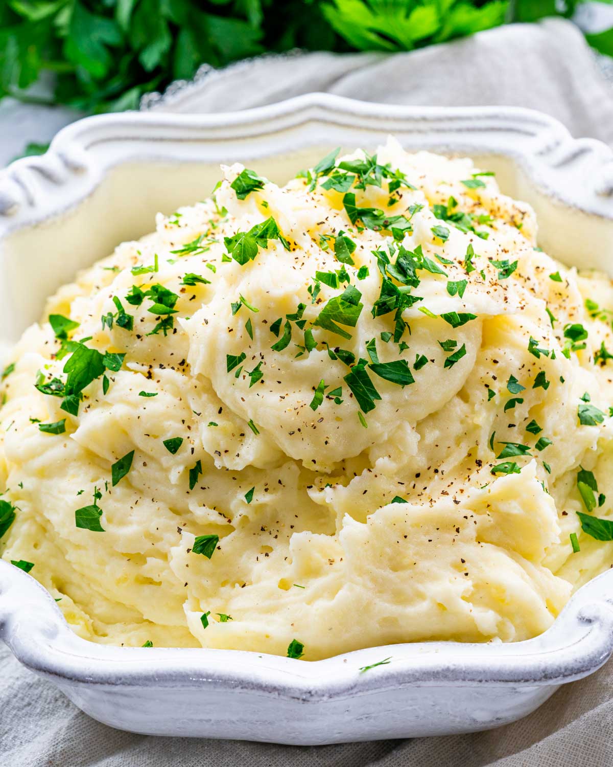 creamy mashed potatoes in a white bowl garnished with parsley.
