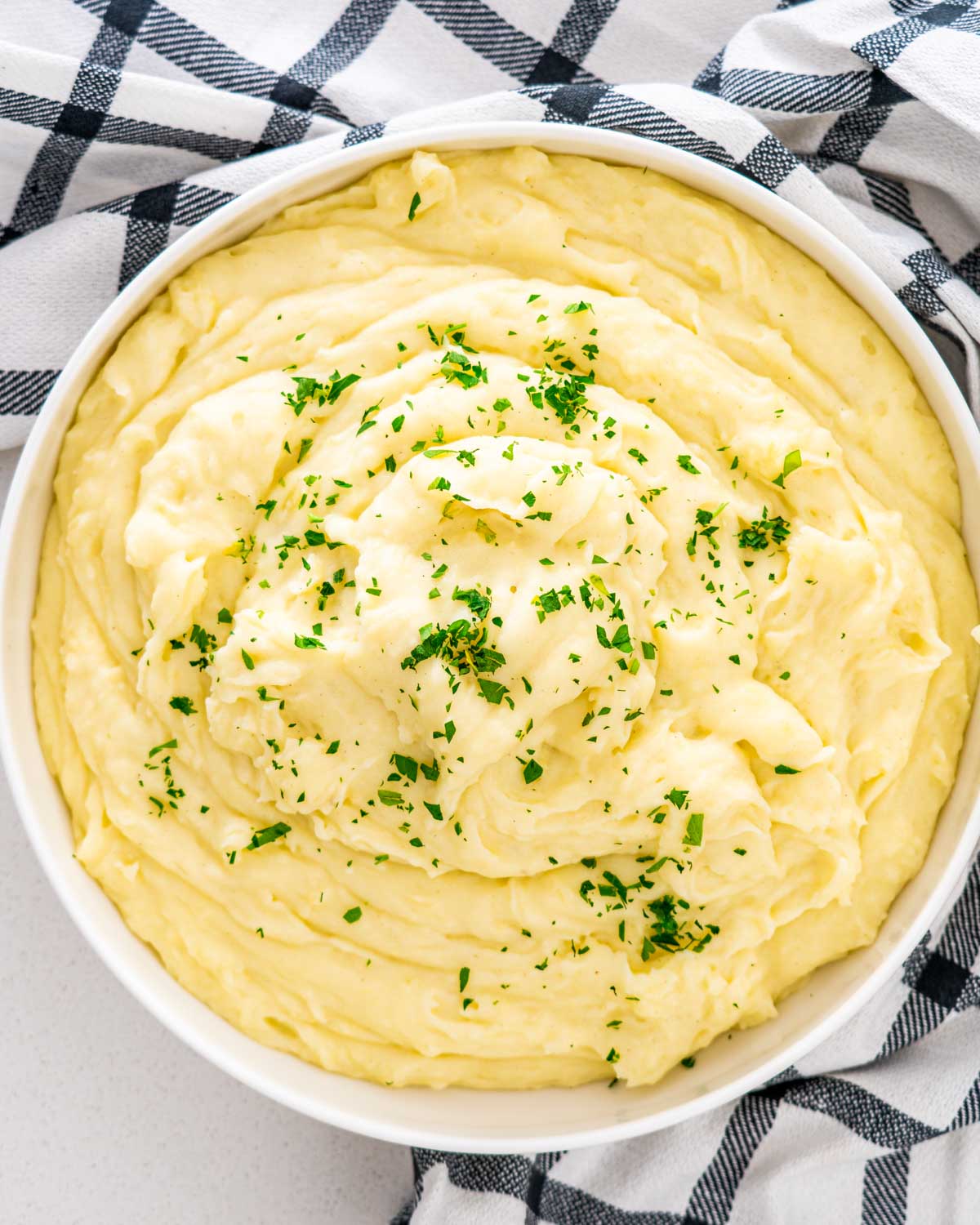 creamy mashed potatoes in a white bowl garnished with parsley.