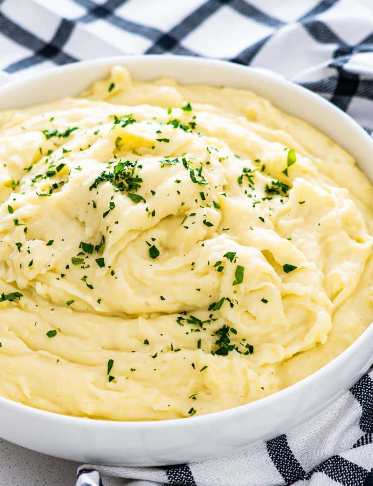 creamy mashed potatoes in a white bowl garnished with parsley.