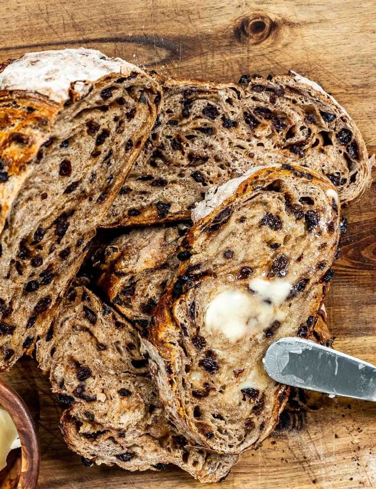 a few slices of no knead cinnamon raisin bread on a cutting board slathered with butter.