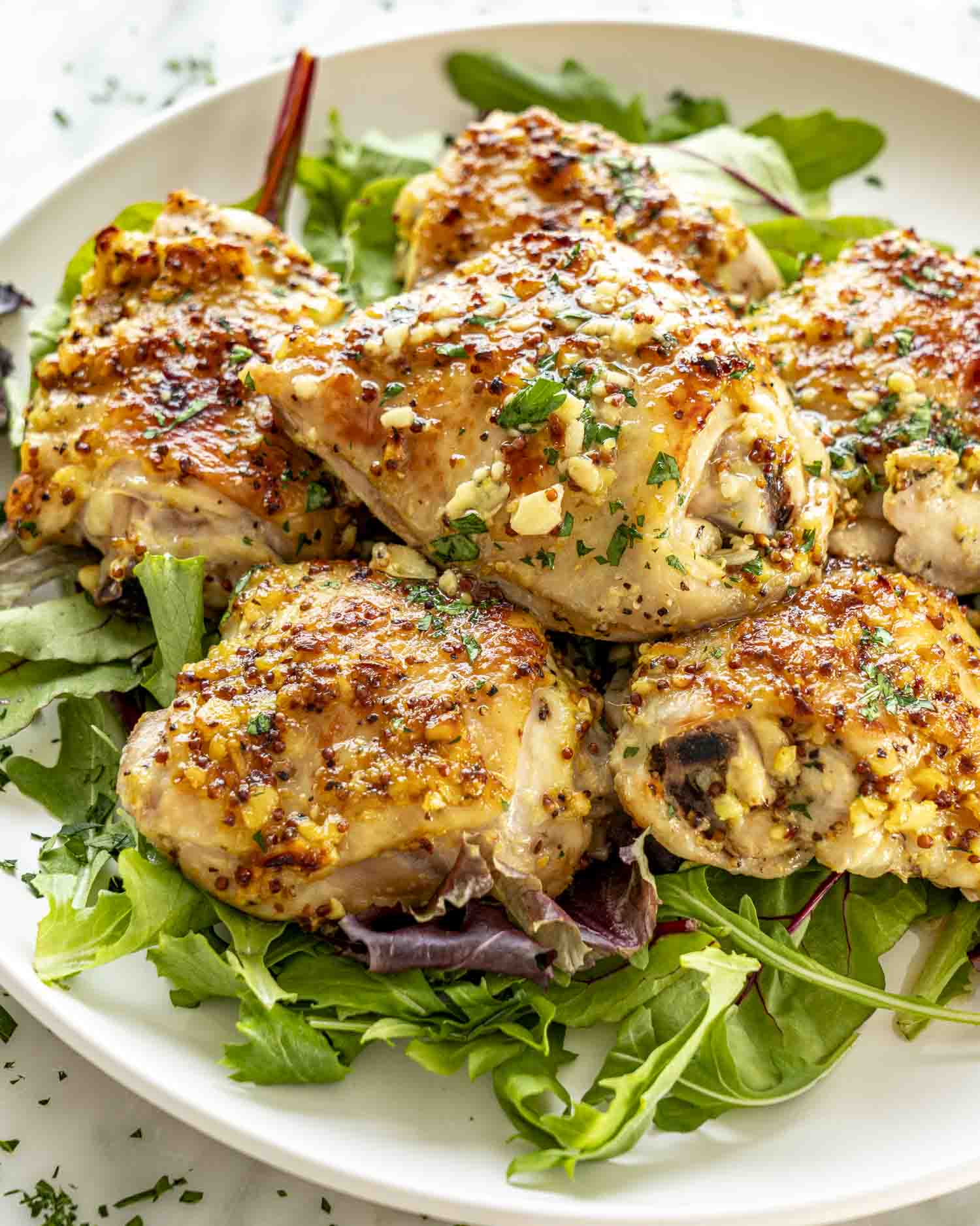 Oven baked chicken thighs served on fresh greens, golden and crispy with visible mustard garlic glaze.