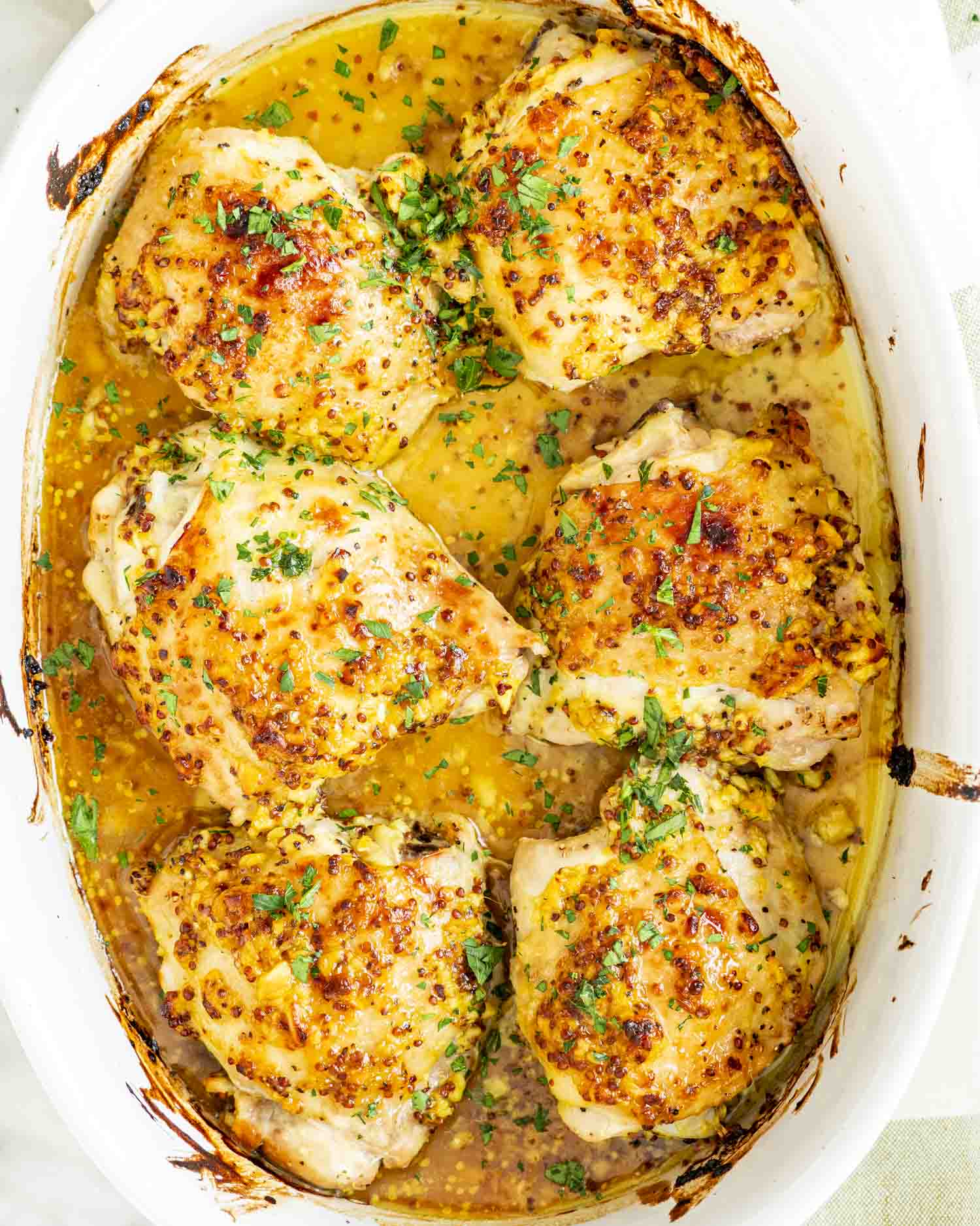 Roasted chicken thighs swimming in rich, golden glaze inside baking dish, topped with parsley and crisped edges.