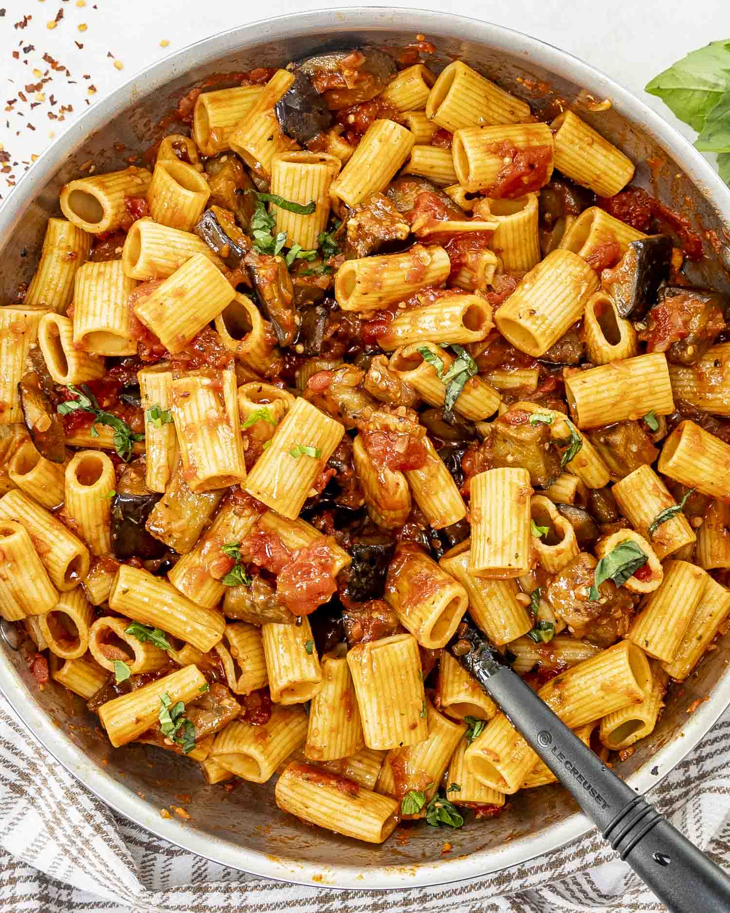 A skillet of Pasta alla Norma featuring rigatoni in a rich tomato sauce with tender eggplant chunks, garnished with fresh basil.