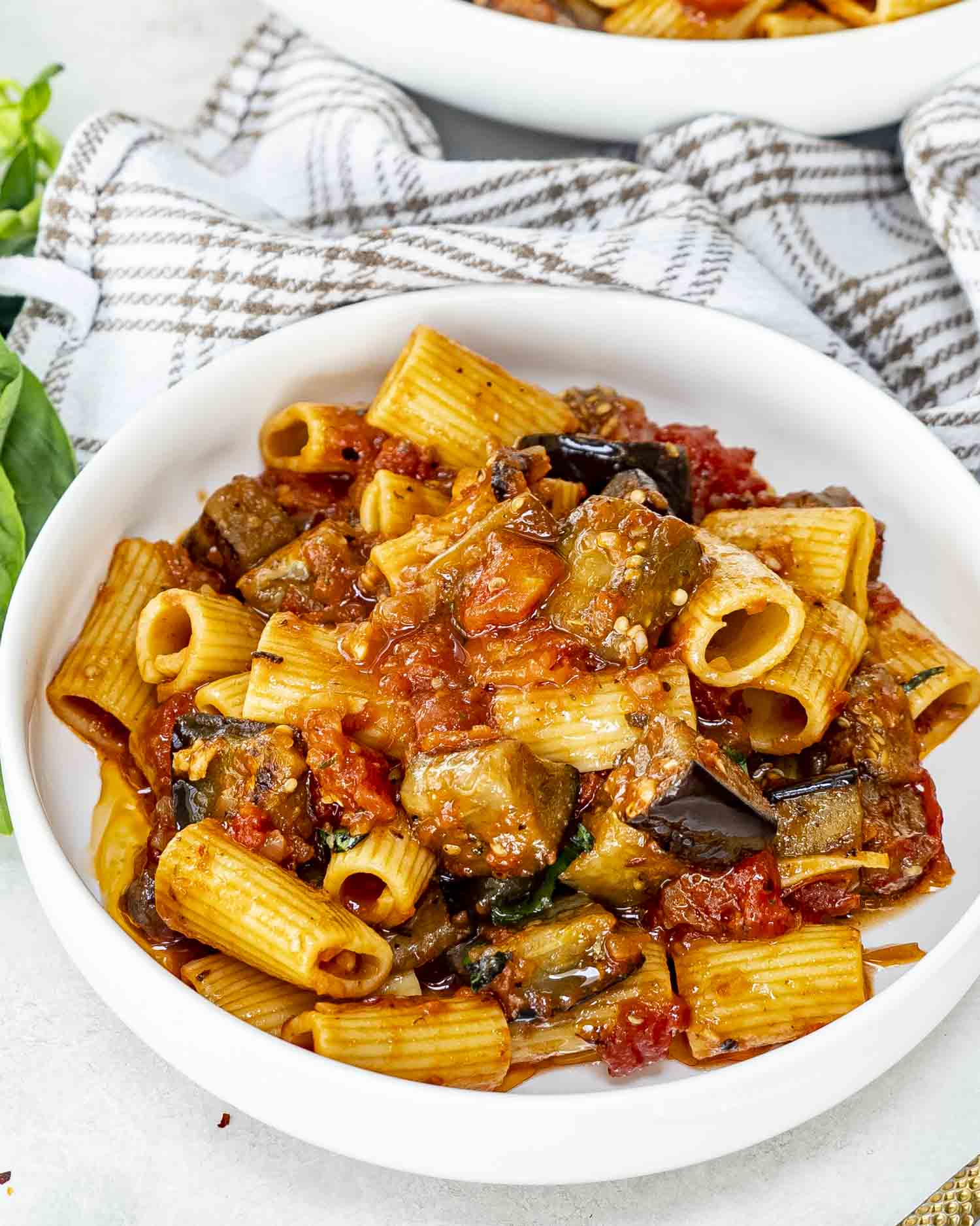 A bowl of Pasta alla Norma featuring rigatoni, tender eggplant chunks, and tomato sauce, garnished with fresh basil leaves.