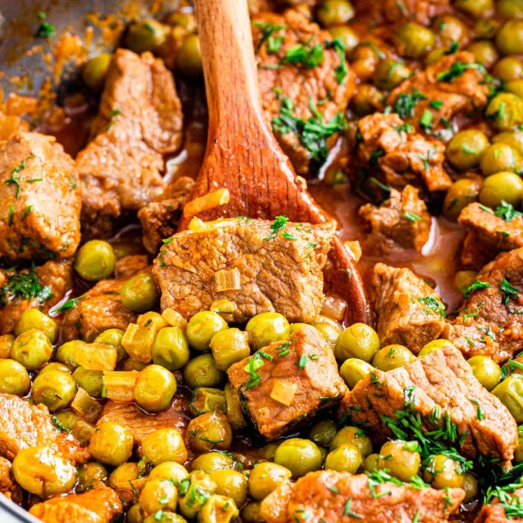 closeup shot of beef and pea stew in a skillet with a wooden spoon inside