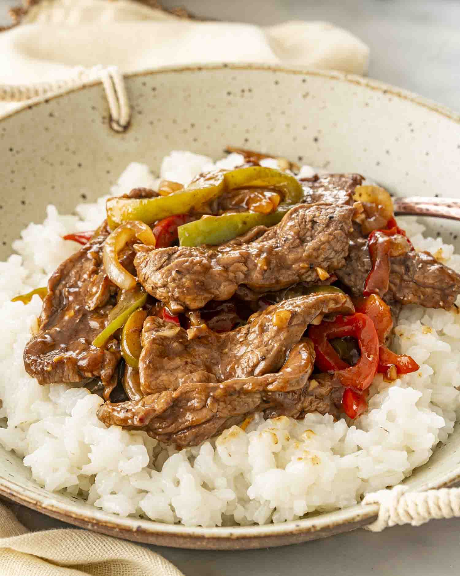 pepper steak over a bed of rice in a bowl.