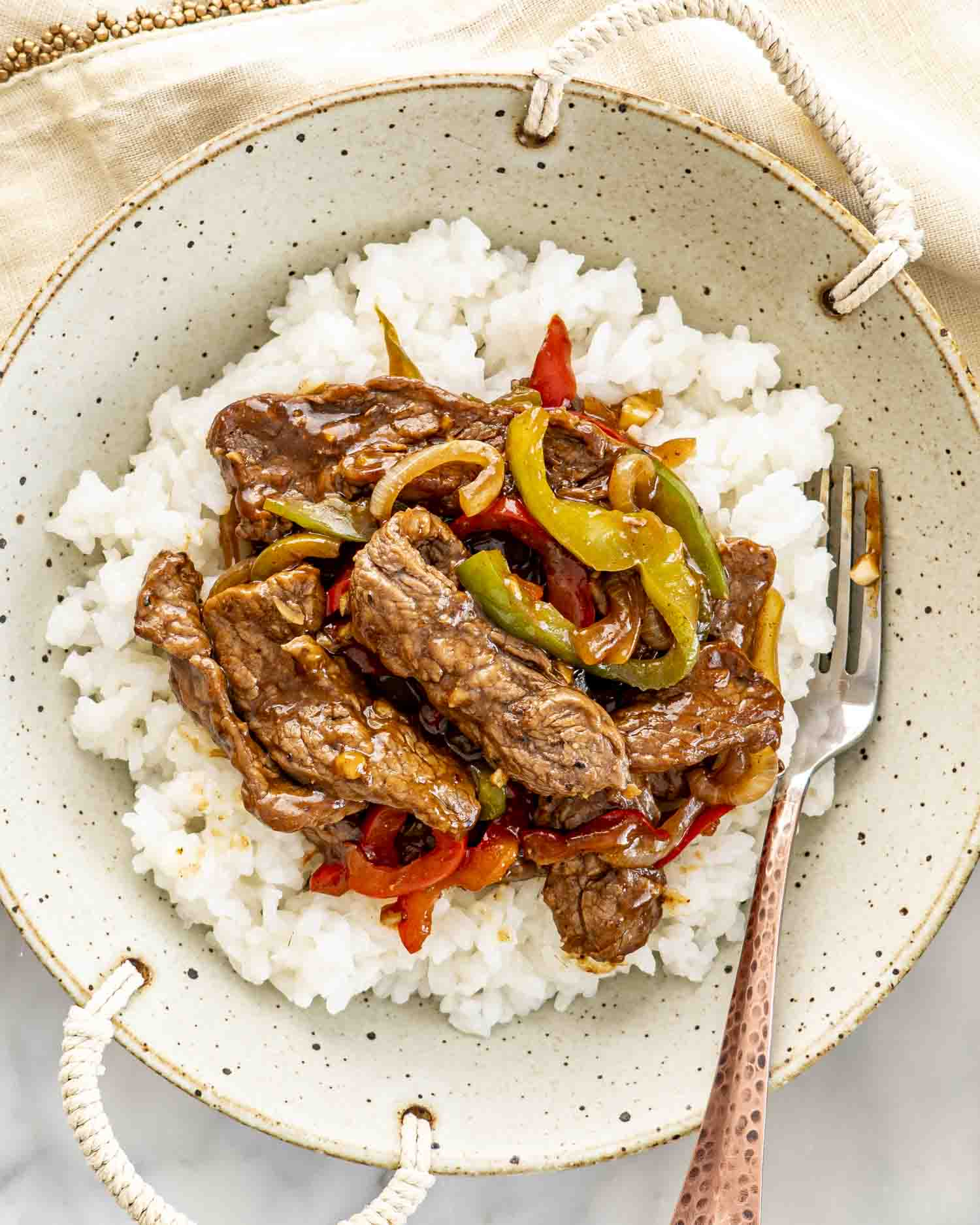 overhead shot of pepper steak over a bed of rice in a bowl.