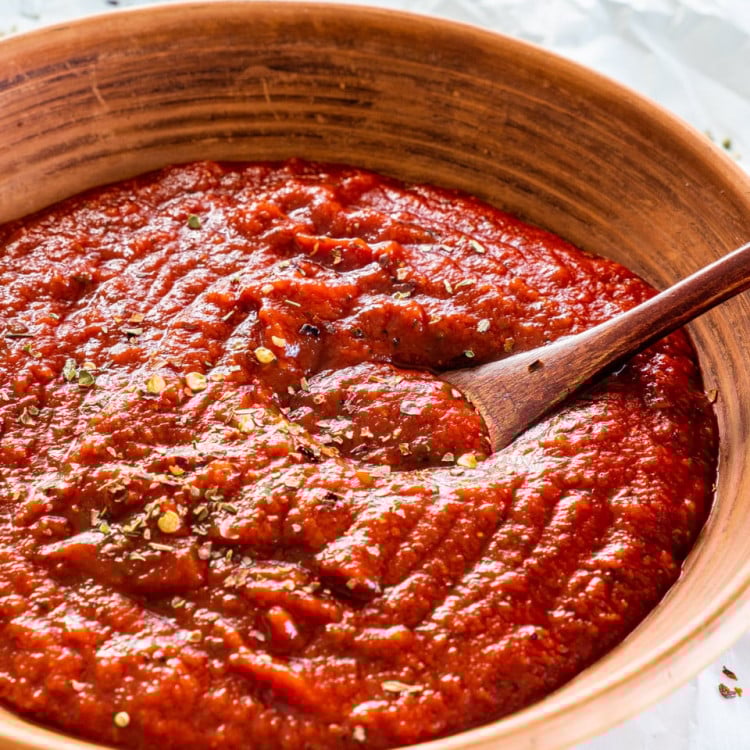 side shot of homemade pizza sauce in a brown plate with a mini wooden spoon in it