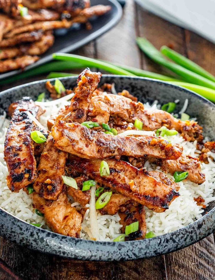 a black plate with rice and pork bulgogi garnished with green onions.