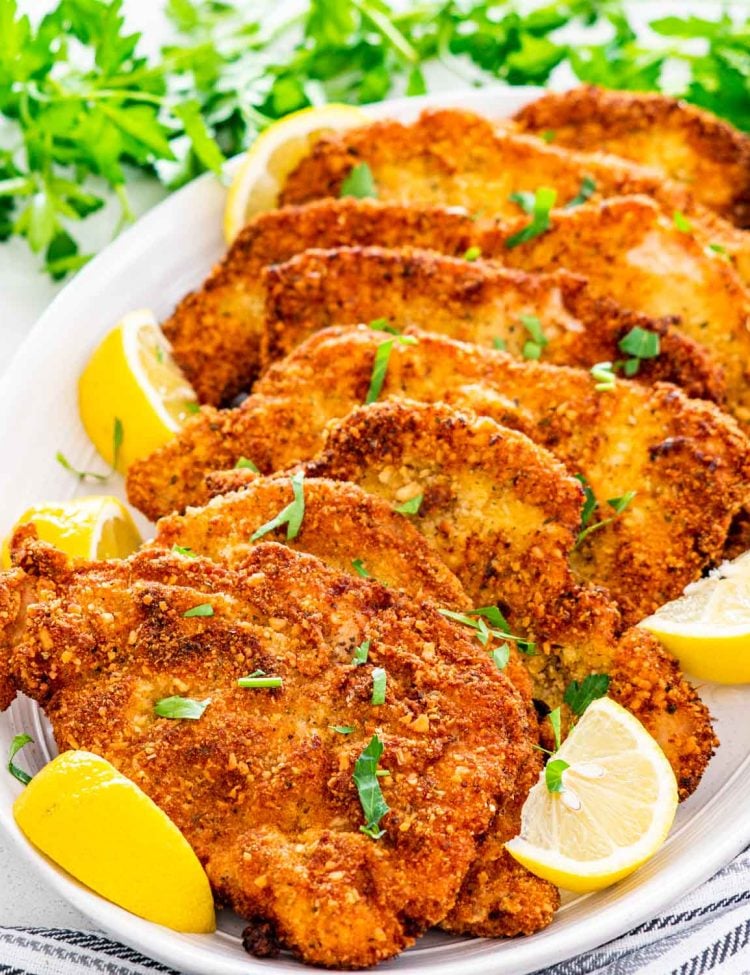 a bunch of pork schnitzel on a serving platter with lemon wedges.
