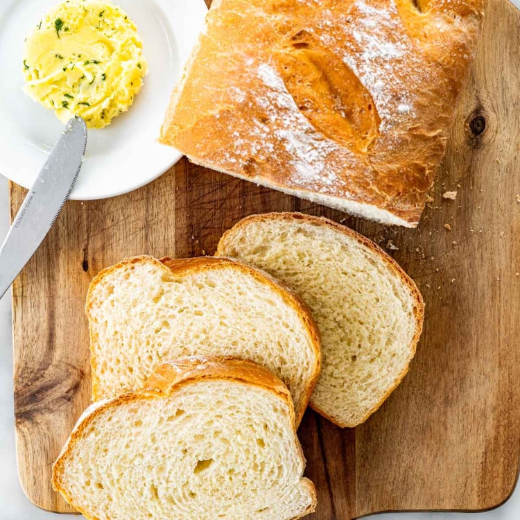 overhead shot of freshly made potato bread on a cutting board with 3 slices a plate with a pat of butter.