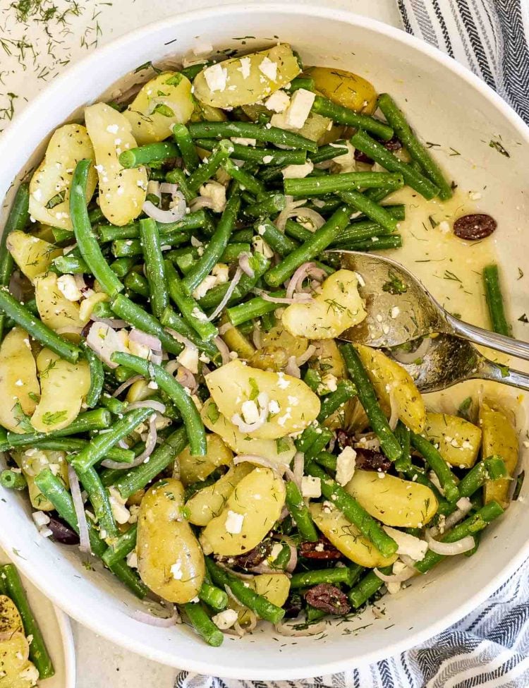 Overhead shot of large mixing bowl filled with lemony potato and green bean salad topped with crumbled feta.