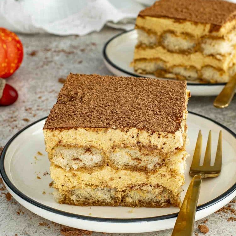 Two square slices of pumpkin tiramisu on plates with golden forks, layered with pumpkin cream and espresso-soaked ladyfingers.
