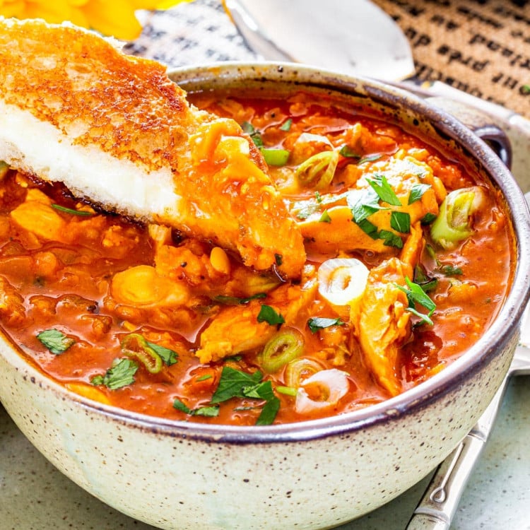 a bowl full of red lentil chicken soup with half a grilled cheese sandwich dipped in the soup