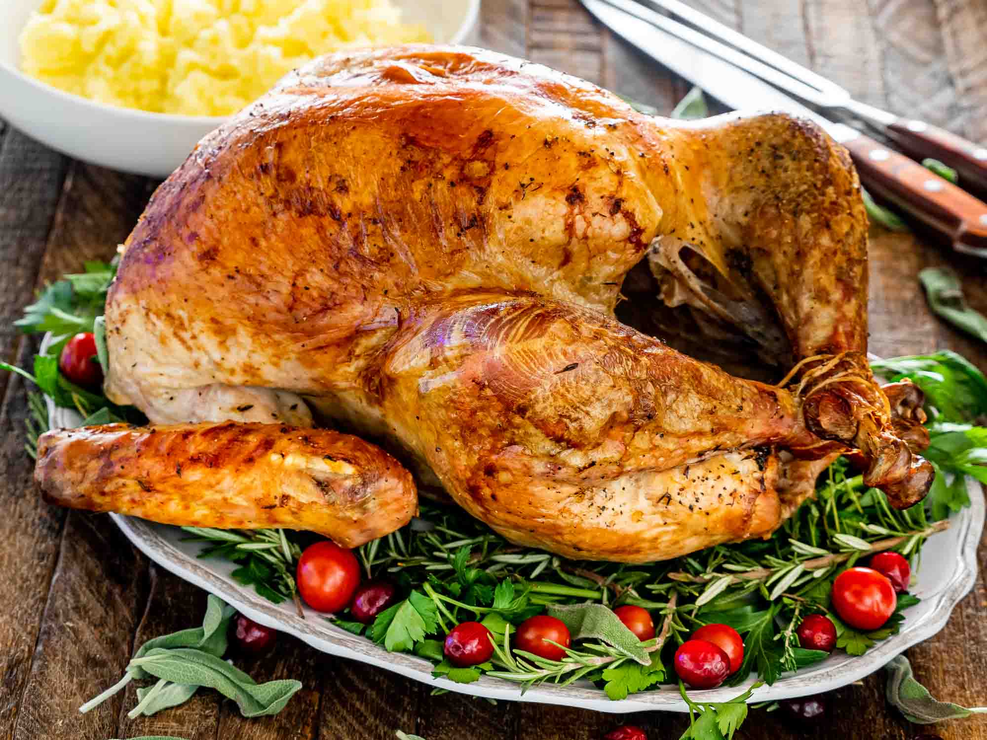 a roast turkey on a turkey platter garnished with herbs and cranberries.