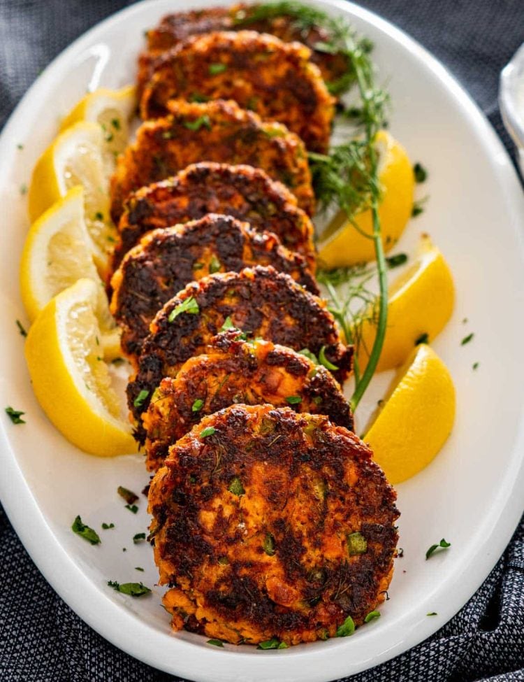 a stack of salmon patties on a serving platter garnished with lemon wedges and dill.