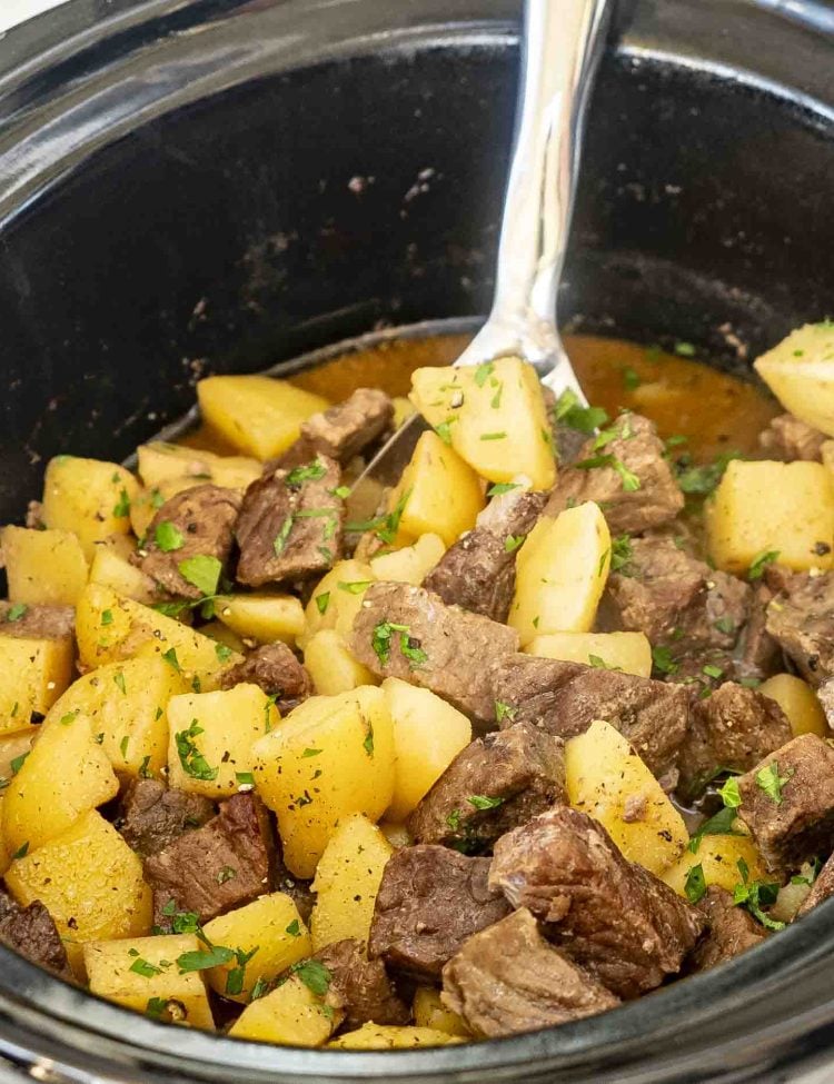 A slow cooker filled with tender beef chunks and golden potato pieces in a savory broth, ready to be served.