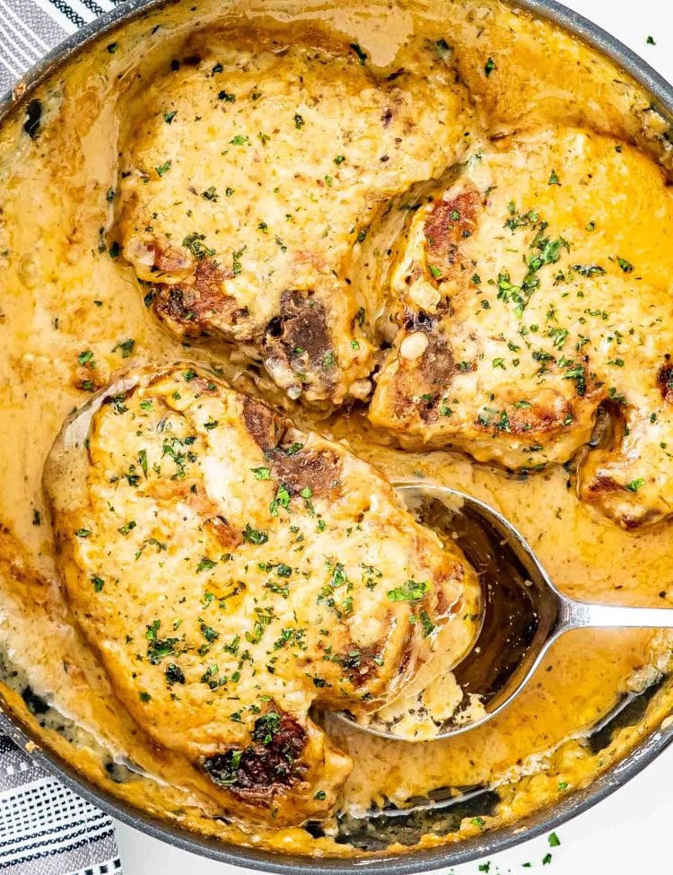 smothered pork chops in a skillet garnished with parsley.
