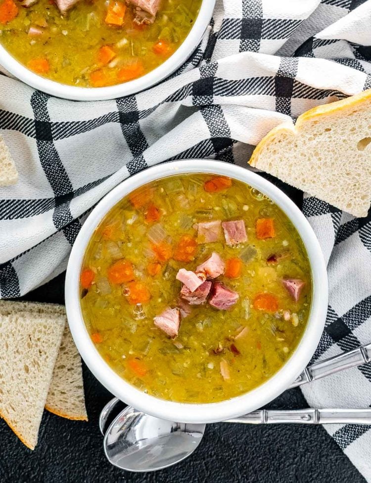 split pea soup in a white bowl with a couple slices of bread around it.