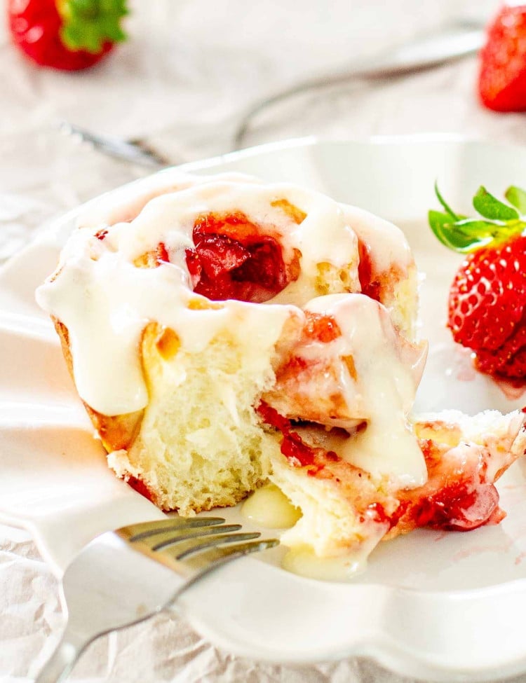 a strawberry roll with cream cheese icing on a white dish.