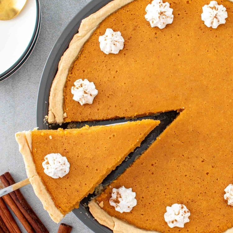 sweet potato pie in a pie plate with a slice being lifted topped with whipped cream.