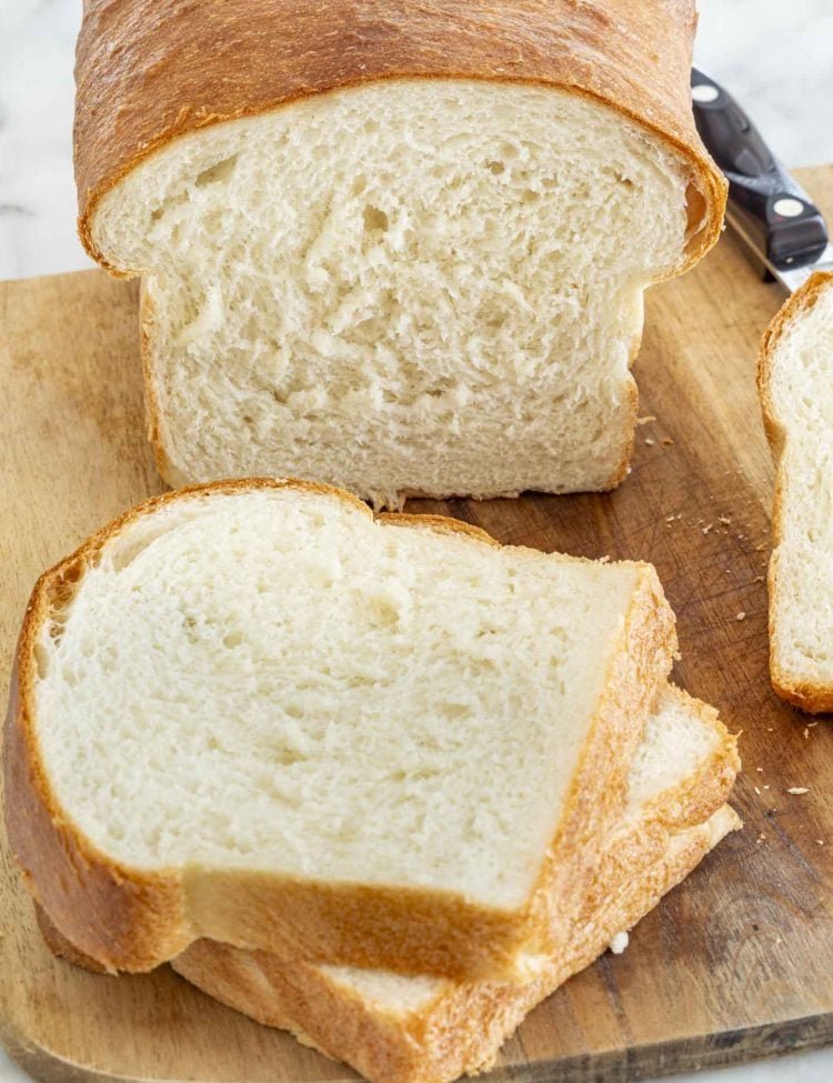 Partially sliced loaf of white bread on a cutting board showing its soft interior and crisp baked crust.